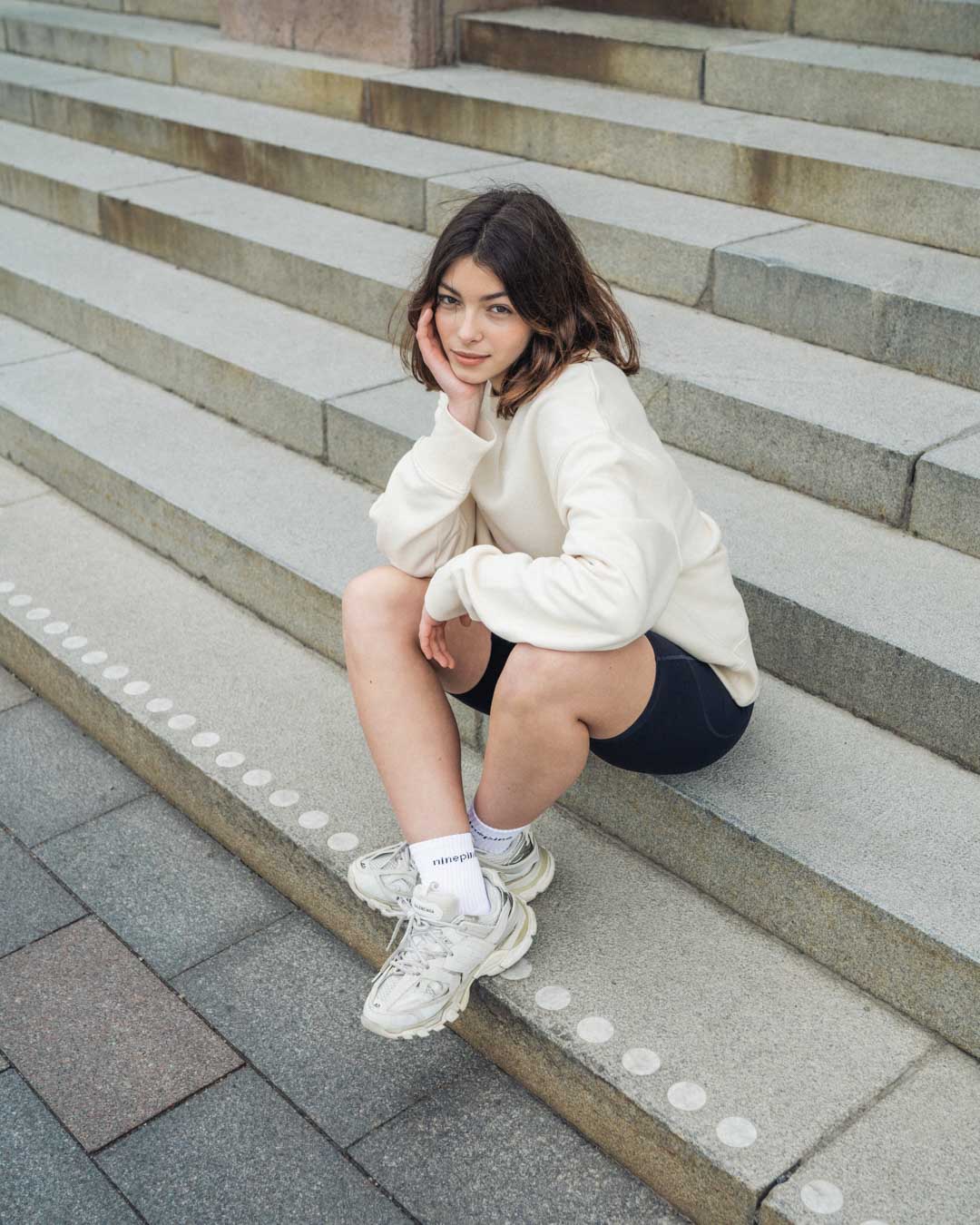 Woman in ninepine sweater and biker shorts setting on sandstone steps