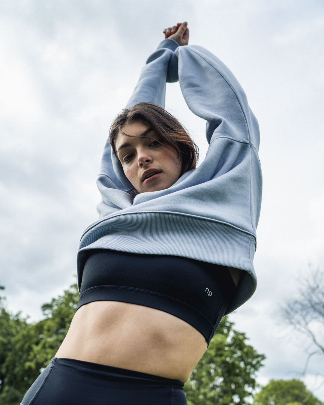 Woman in a park stretching with her hands in the air in her ninepine sweater