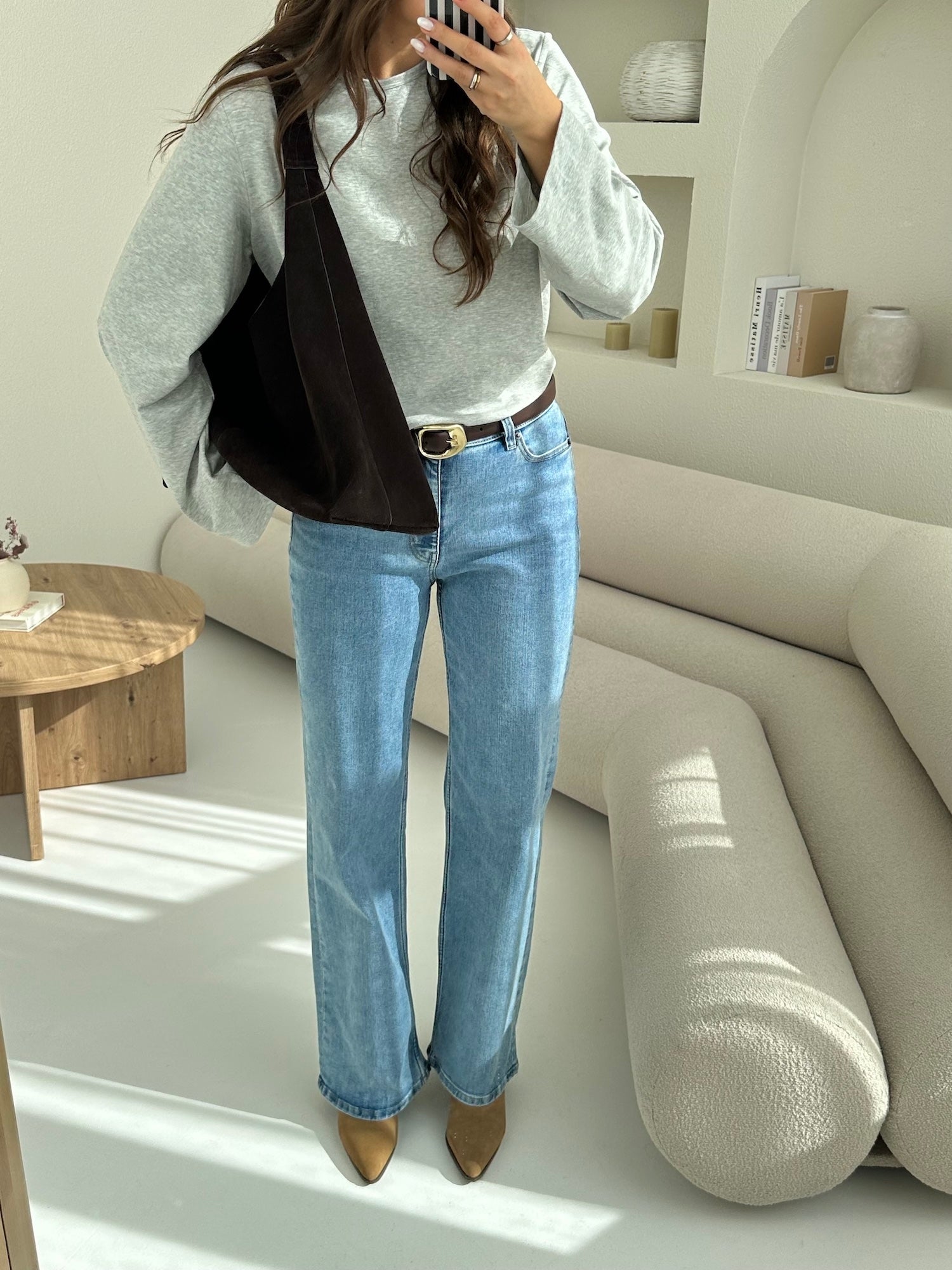Woman wearing light blue Relaxed ComfortDenim jeans and a heather grey Pima long-sleeve T-shirt styled with a dark shoulder bag and minimalist accessories.